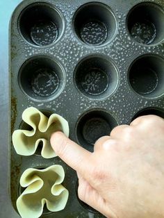 a person is pointing at some food in a muffin tin with cupcake holes