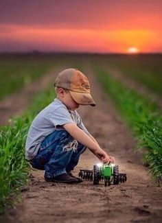 a little boy is playing with toy trucks in the middle of a field at sunset