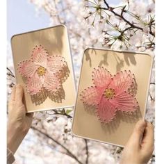 two pink flowers are being held up in front of some cherry blossoming tree branches