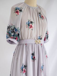 Embark on a journey of vintage elegance with our Sugar Cream Vintage midi dress. Crafted from delicate chiffon in pristine white, it features a round neck with back zippers and elegant half sleeves.   Adorned with a colorful mini floral bouquet print and wide floral border, it exudes charm and whimsy. Complete with an elasticated waist and fabric belt with a golden buckle, it's the perfect embodiment of unique, ethical fashion. Care: Cool machine wash. Dry at a lower heat and press with a medium iron.  Condition: Embrace the distinctive charm of this upcycled treasure, where imperfections are unique features. Delight in the occasional loose thread or subtle discoloration, each adding to the character and history of this special garment. Vintage Cream Dress With Floral Print, Vintage Knee-length Floral Print Dress, Vintage Floral Print V-neck Dress, Multicolor Embroidered V-neck Dress With Floral Print, Vintage Midi Dress, Retro Vintage Floral Print V-neck Dress, Vintage Midi Dresses, Chiffon Midi Dress, Vintage Elegance