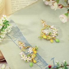 Brighten up your style with our Lemon Garland Earrings! These delightful accessories capture the freshness of a garden and the carefree spirit of a vacation. Crafted with meticulous detail, each earring showcases a cluster of vibrant lemons, creating a playful and joyful look. Elevate your ensemble with this cheerful and nature-inspired accessory. 🍋🌿🌞 DETAILS Plating: 18K Gold  Materials: 18K Gold on Brass,   Enamel, Cubic Zirconia Size: 1.69"* 1.22 "(4.3cm*3.1cm) Weight:12.4g/pr Whimsical Spring Jewelry Gift, Spring Flower Charm Hoop Earrings As Gift, Spring Flower Dangle Earrings, Spring Hoop Earrings With Flower Charm As Gift, Spring Gift Hoop Earrings With Flower Charm, Flower-shaped Jewelry With Matching Earrings For Spring, Whimsical Flower Jewelry For Spring, Bohemian Jewelry With Flower Decoration For Summer, Summer Gift Jewelry With Flower Decoration