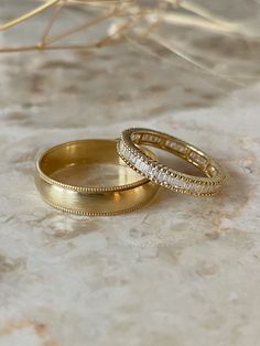 two gold wedding rings sitting on top of a marble surface