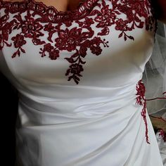 a woman in a white wedding dress with red flowers on her shoulder and veil around her neck