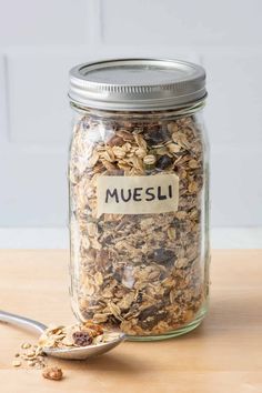 a glass jar filled with granola on top of a wooden table next to a spoon