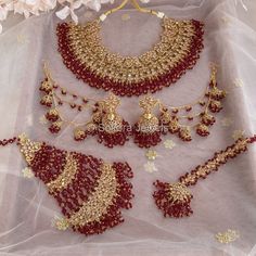 a red and gold jewelry set on a white tablecloth with flowers in the background