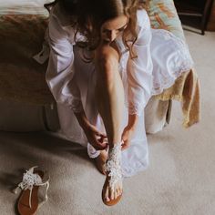 a woman in white dress sitting on the floor next to her wedding shoes and sandals