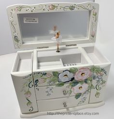 an ornate white box with flowers painted on the front and sides, holding a figurine