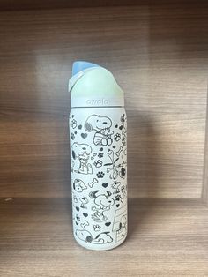 a baby bottle sitting on top of a wooden shelf next to a wall with drawings