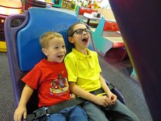 two young boys sitting on top of a blue chair in a play room with toys