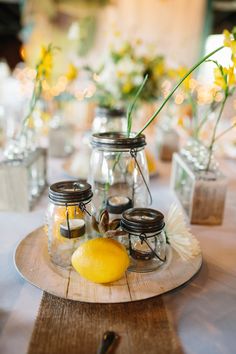 mason jars filled with lemons and flowers on a wooden tray at a wedding reception