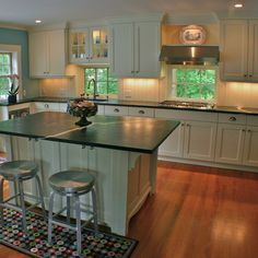 a large kitchen with white cabinets and black counter tops on hardwood flooring, along with two bar stools at the center island