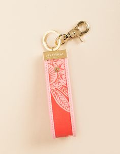 a pink keychain with an orange and white design on the front is attached to a gold metal hook