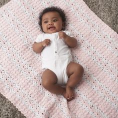 a baby laying on top of a pink crocheted blanket next to a gray carpet