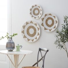 three woven plates hang on the wall above a table with a vase and two chairs