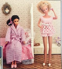 two barbie dolls sitting on a bed next to each other, one in a pink robe and the other in a white dress