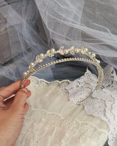 a woman is holding a tiara with pearls and beads on it, while wearing a wedding dress