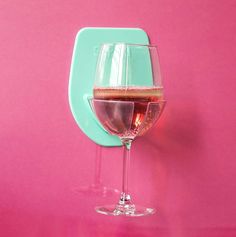 a glass of wine sitting on top of a pink counter next to a green holder