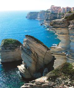 an ocean cliff overlooks the blue water and buildings in the distance, along with cliffs on either side