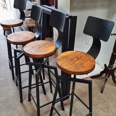 four stools with wooden seats are lined up on the floor in front of a wall