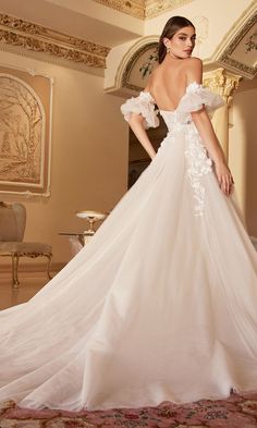 a woman in a white wedding dress with flowers on the back and shoulder, standing near a mirror