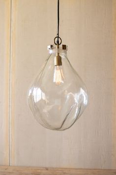 a clear glass light hanging from a metal hook on a wooden table with a white wall in the background