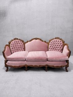 a pink velvet couch with ornate carvings on the back and arms, in front of a gray wall