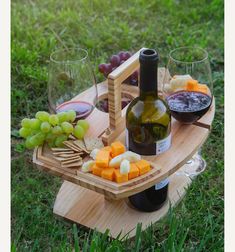 a bottle of wine, cheese and grapes on a wooden platter in the grass