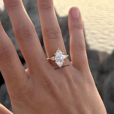 a woman's hand with an engagement ring on top of her finger and the ocean in the background