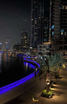 the city is lit up at night with blue lights and palm trees in front of it