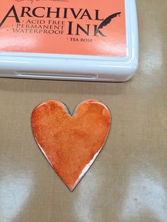 an orange heart shaped brooch sitting on top of a table next to a tea box