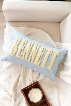 a blue pillow with the word bennet on it next to a candle and a box