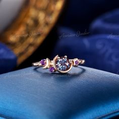 a ring with three stones on it sitting on top of a blue cushion