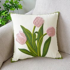 a white pillow with pink tulips embroidered on the front and green leaves in the back