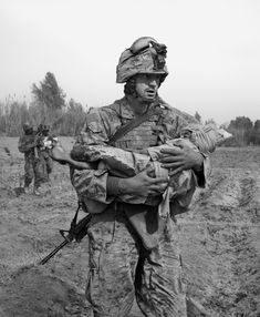 black and white photograph of soldiers carrying an injured soldier in the mud, with another man walking behind them