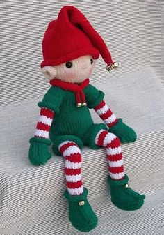 a knitted elf doll sitting on top of a white couch wearing green and red striped socks