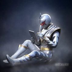 a man in silver and gold sitting on the ground with his legs crossed, holding a tablet