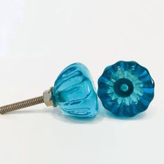 two blue glass knobs are on a white surface and one has a screw in the middle