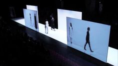 several images are projected on the wall in front of people walking down the catwalk