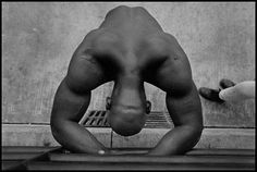 a naked man standing in front of a wall with his hands behind his head and feet on the ground