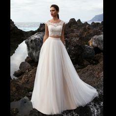 a woman in a wedding dress standing on rocks by the ocean with her hands behind her back