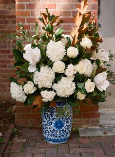 a blue and white vase with flowers in it on a brick floor next to a brick wall