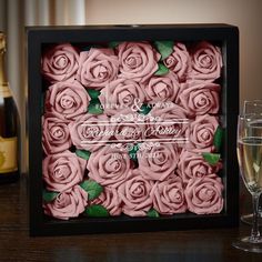 pink roses are in a black box with wine glasses next to it and two champagne flutes