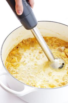 a person mixing food in a pot with a blender on the side and a spoon sticking out of it