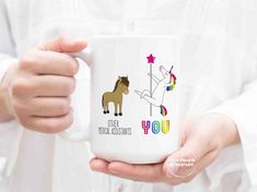 a person holding a coffee mug with an unicorn, horse and rainbow on it's side