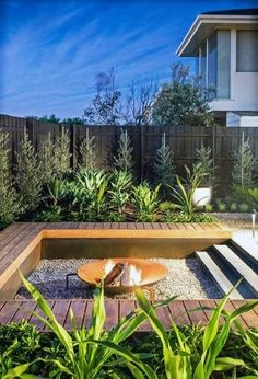 an outdoor fire pit surrounded by greenery and plants in front of a fenced backyard