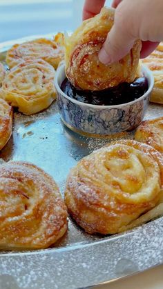 a person dipping some food into a bowl on top of a metal tray with other pastries