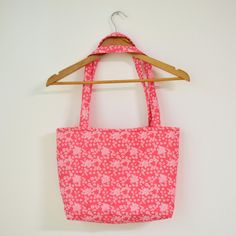 a pink flowered bag hanging on a wooden hanger next to a white wall