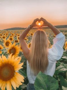 a woman standing in a sunflower field holding her hands up to the heart shape