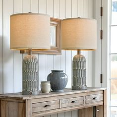 two lamps sitting on top of a wooden table next to a mirror and lamp shade