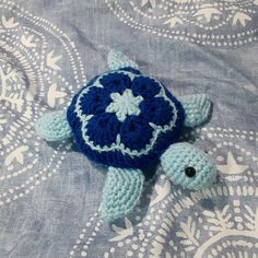 a small crocheted turtle laying on top of a blue and white bed sheet